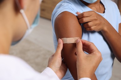 Photo of Doctor putting adhesive bandage on young woman's arm after vaccination indoors, closeup
