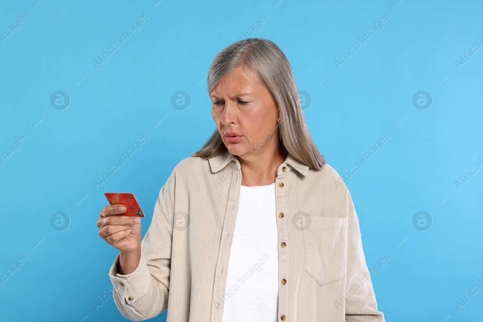 Photo of Worried woman with credit card on light blue background. Be careful - fraud