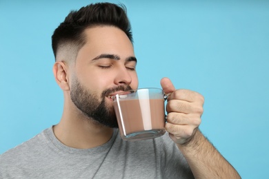 Young man drinking chocolate milk on light blue background