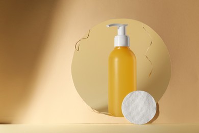 Photo of Hole with face cleansing product and cotton pad on beige background