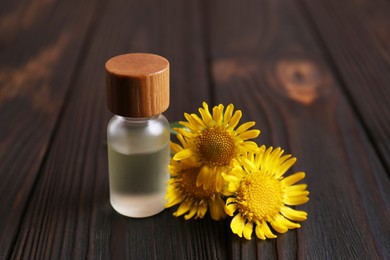 Photo of Glass bottle of aromatic essential oil and yellow wildflowers on wooden table, closeup