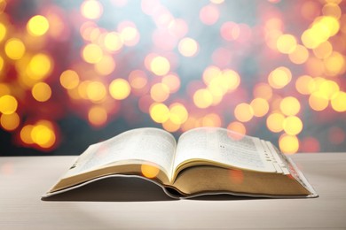 Open Bible on wooden table, bokeh effect