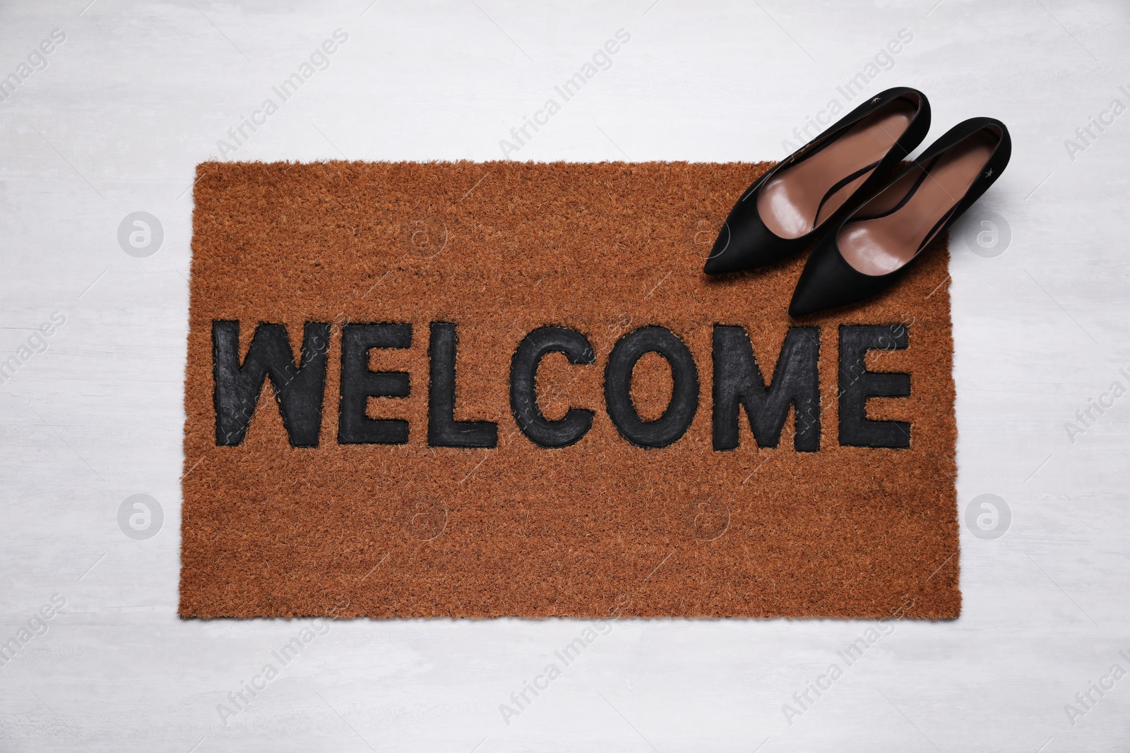 Photo of New clean mat with word WELCOME and shoes on floor, top view