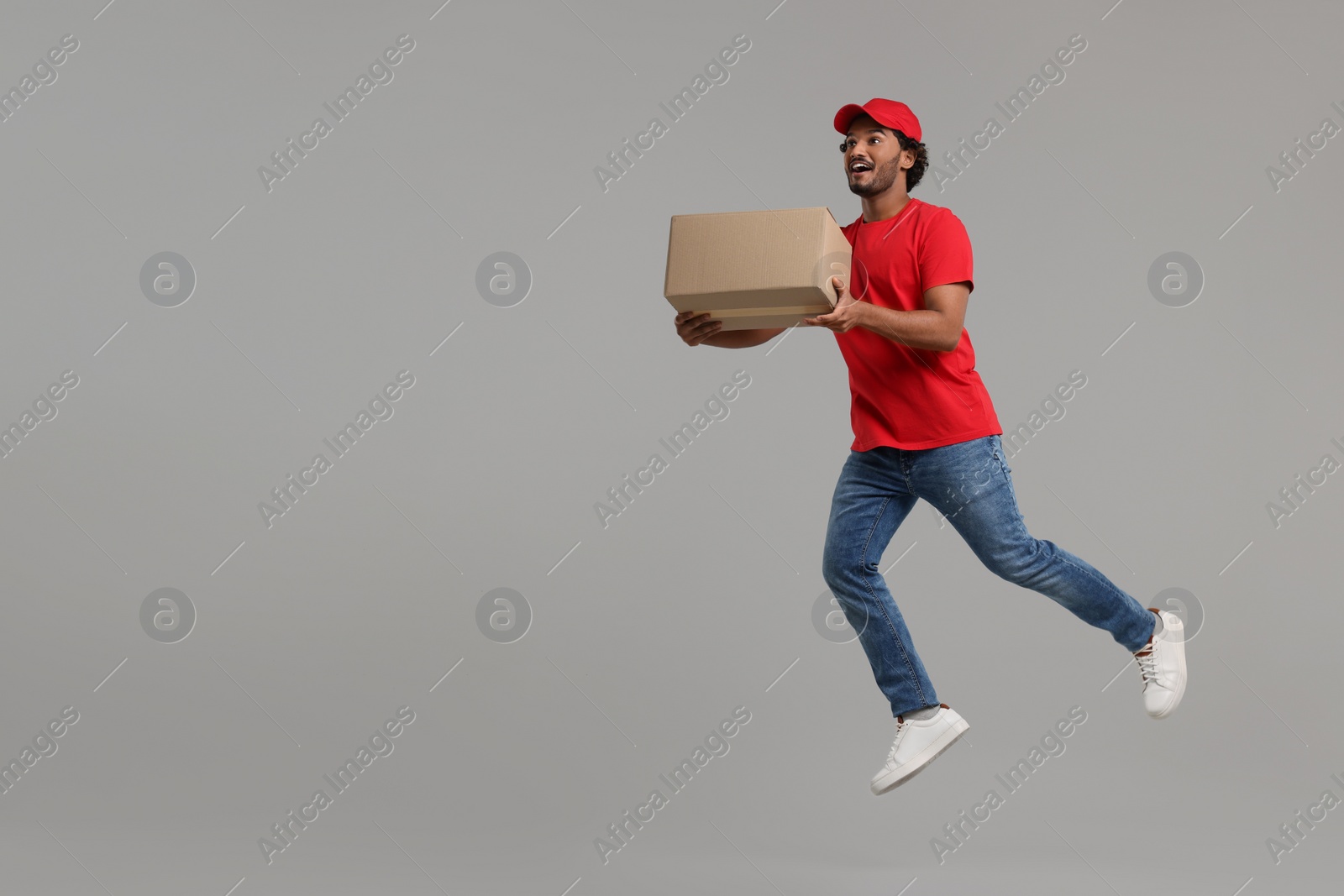 Photo of Happy courier with parcel jumping on grey background, space for text