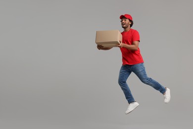 Happy courier with parcel jumping on grey background, space for text