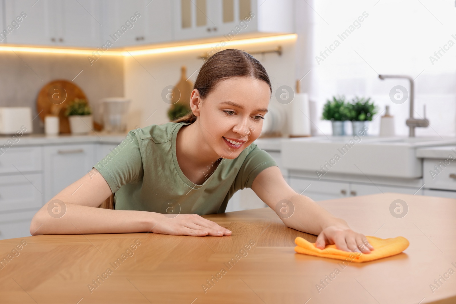 Photo of Woman with microfiber cloth cleaning wooden table in kitchen