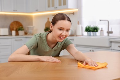 Photo of Woman with microfiber cloth cleaning wooden table in kitchen