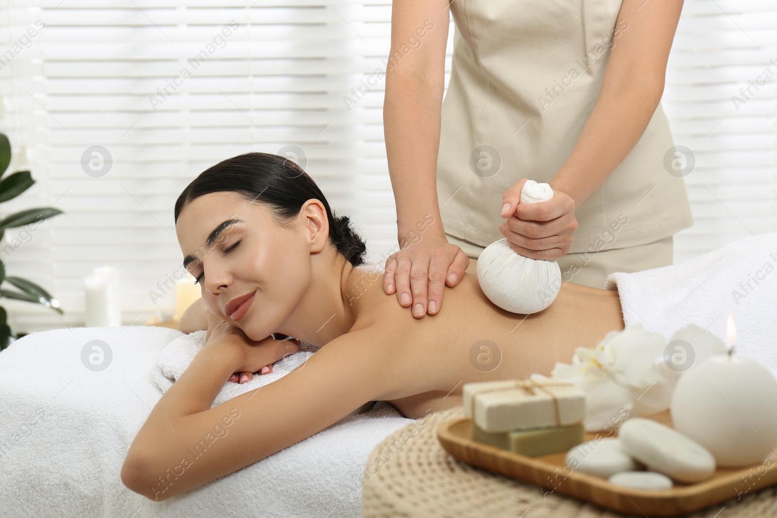 Photo of Young woman receiving herbal bag massage in spa salon