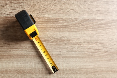 Metal measuring tape on wooden background, top view. Space for text