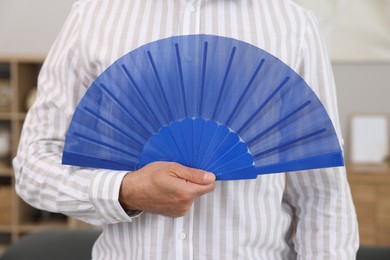 Man with blue hand fan at home, closeup