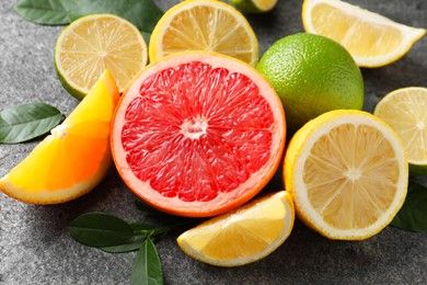 Different fresh citrus fruits and leaves on grey textured table, closeup