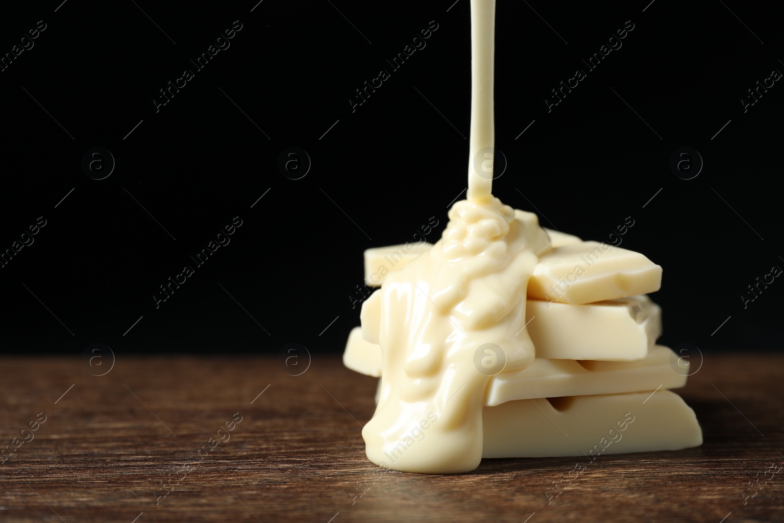 Photo of Pouring tasty white chocolate paste onto pieces on wooden table, closeup. Space for text