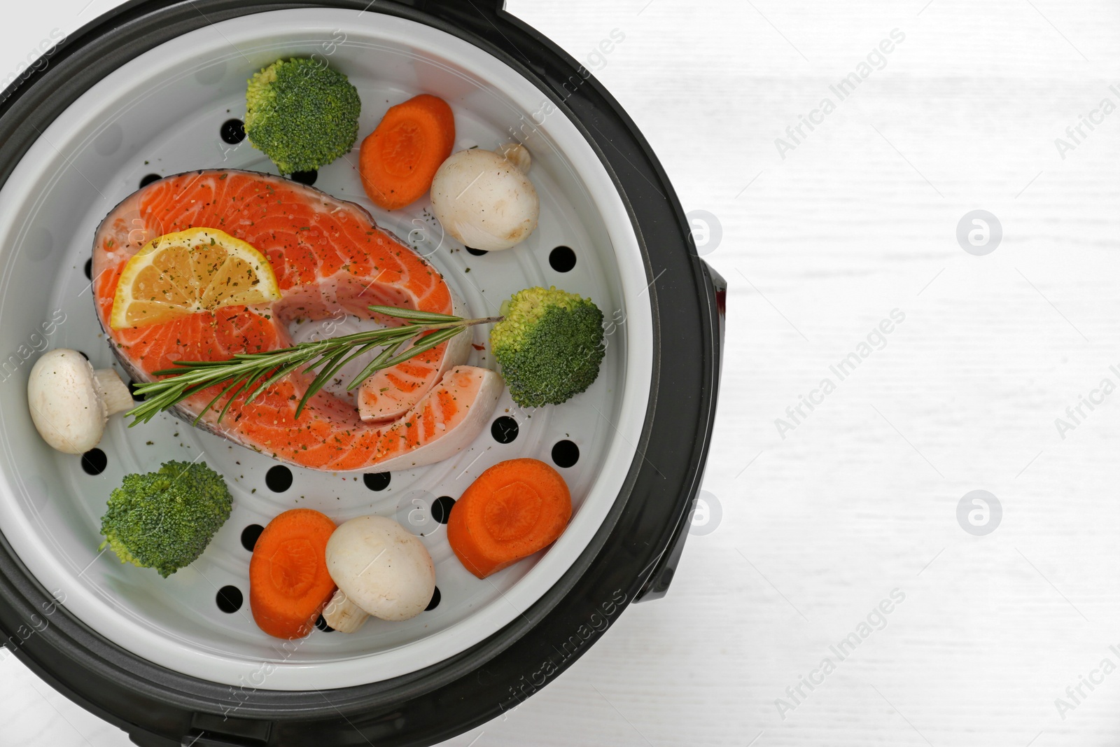 Photo of Salmon steak with garnish in multi cooker on white wooden table, top view