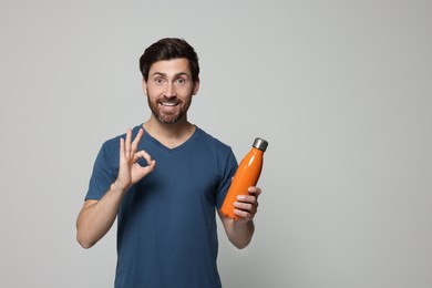 Man with orange thermo bottle showing ok gesture on light grey background. Space for text