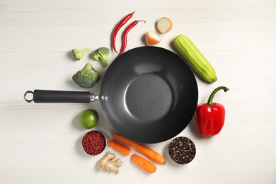 Photo of Empty iron wok surrounded by raw ingredients on white wooden table, flat lay