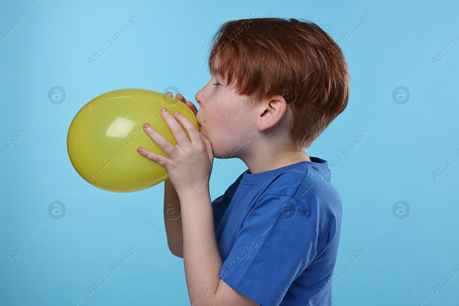 Photo of Boy inflating yellow balloon on light blue background