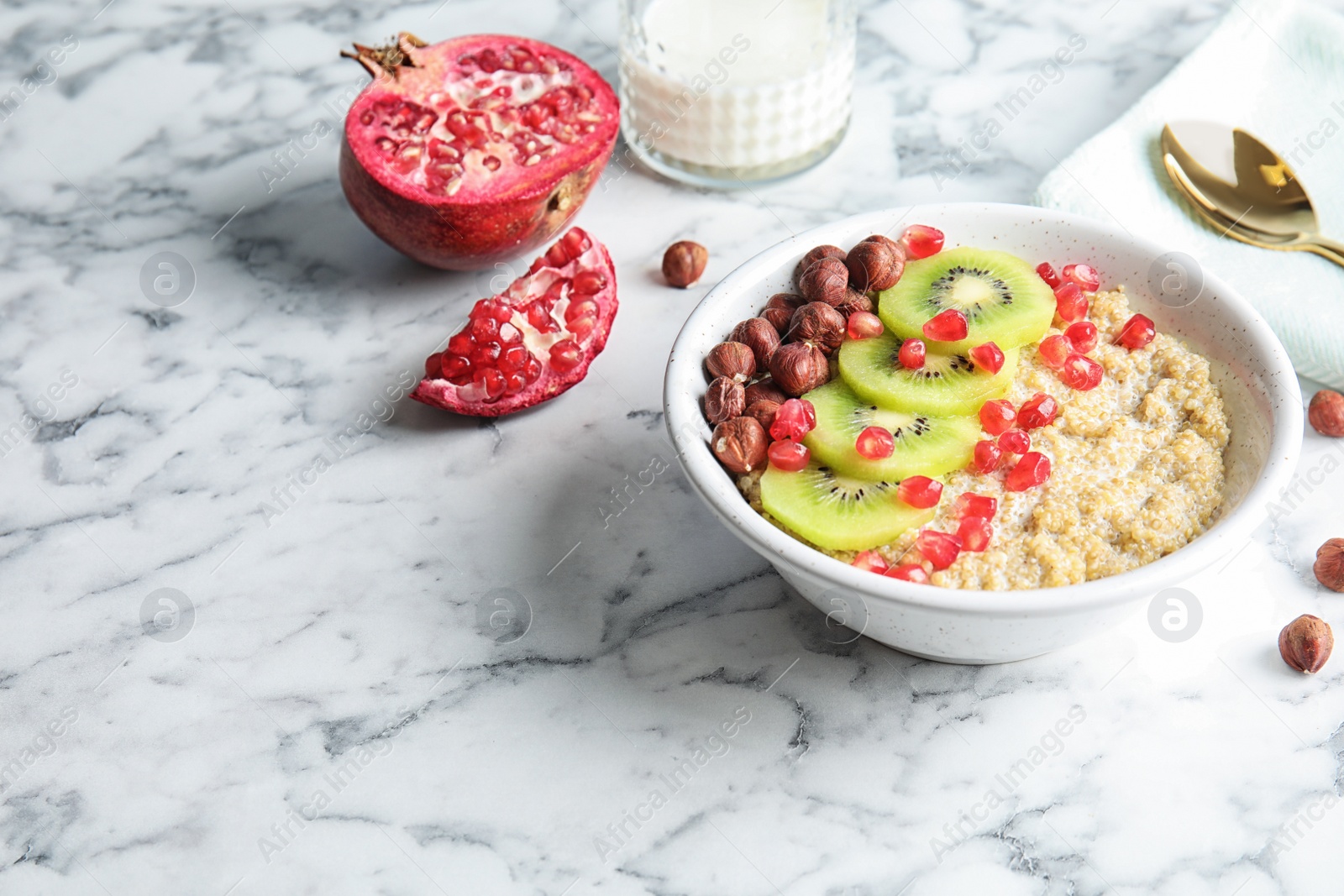 Photo of Bowl of quinoa porridge with hazelnuts, kiwi and pomegranate seeds served for breakfast on marble table. Space for text