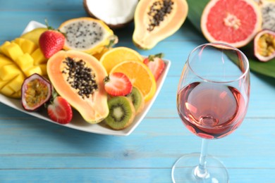 Photo of Delicious exotic fruits and glass of wine on light blue wooden table