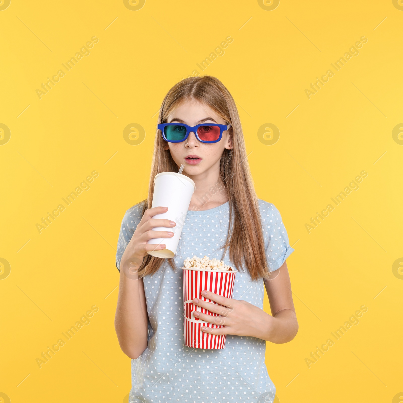 Photo of Emotional teenage girl with 3D glasses, popcorn and beverage during cinema show on color background