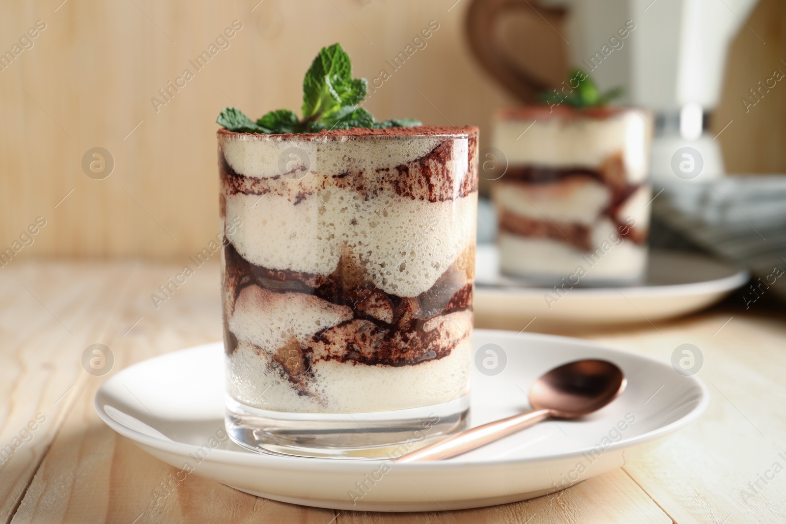 Photo of Tasty tiramisu and mint in glass on light wooden table, closeup