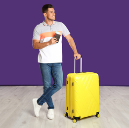 Handsome man with suitcase and ticket in passport for summer trip near purple wall. Vacation travel