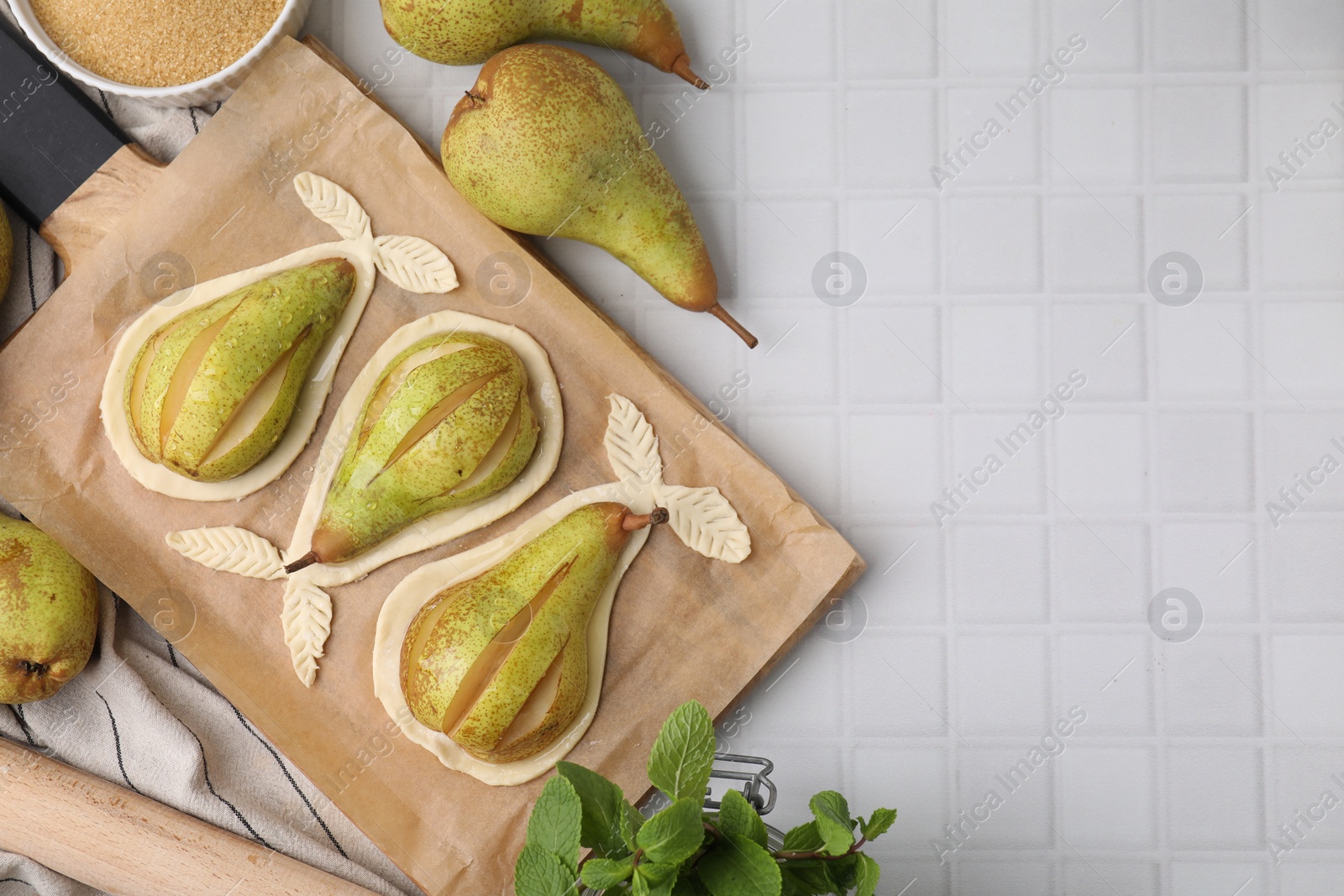 Photo of Board with raw dough, fresh pears and mint on white tiled table, flat lay. Space for text