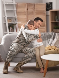 Young man in military uniform with his little son on sofa at home