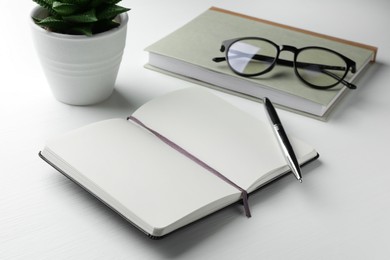 Photo of Different notebooks, pen, glasses and plant on white wooden table