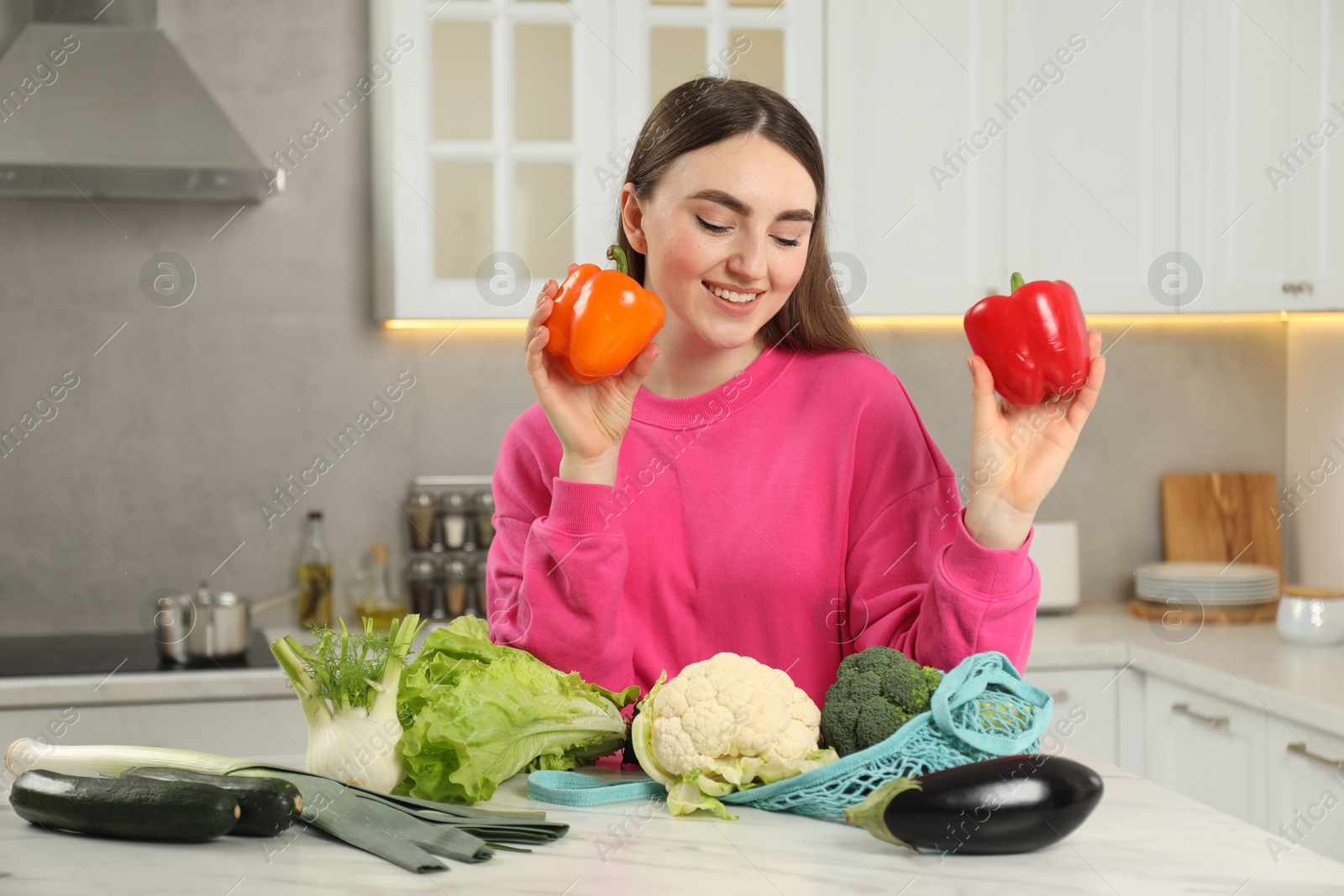 Photo of Woman with peppers and string bag of vegetables at light marble table in kitchen