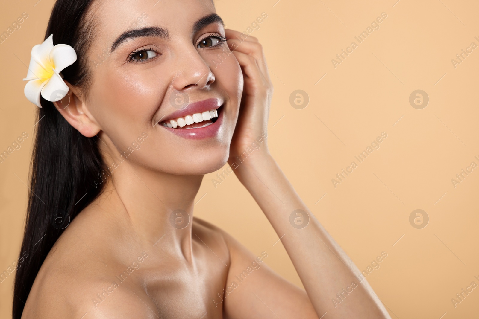 Photo of Young woman with plumeria flower in hair on beige background, space for text. Spa treatment