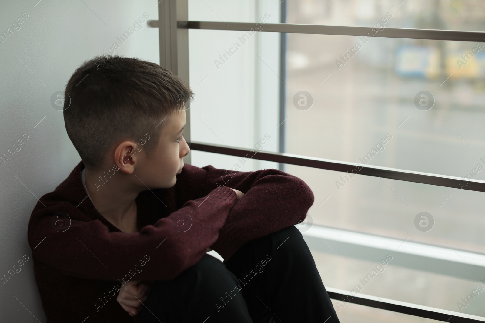 Photo of Upset boy sitting near window indoors. Space for text