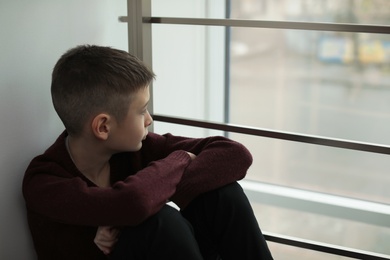 Photo of Upset boy sitting near window indoors. Space for text