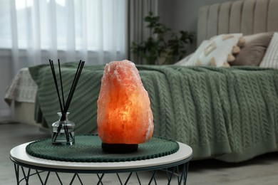 Photo of Beautiful Himalayan salt lamp and air reed freshener on table in bedroom, space for text