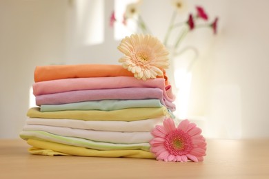 Photo of Stack of clean clothes and flowers on wooden table