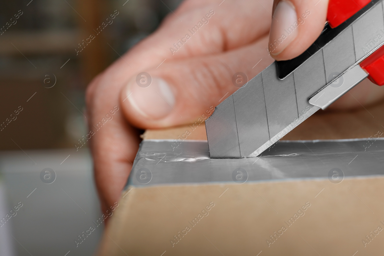 Photo of Man using utility knife to open parcel, closeup