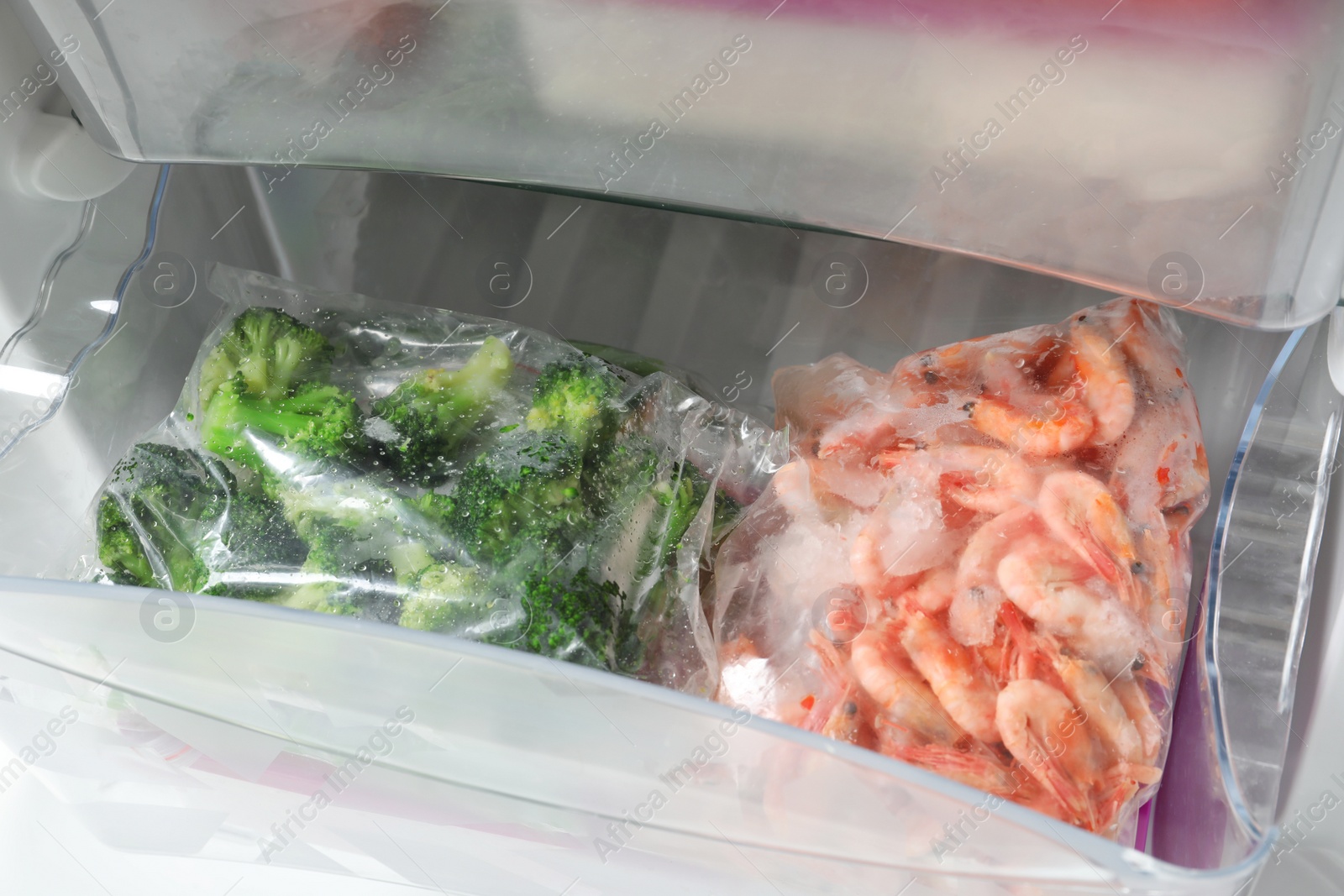 Photo of Plastic bags with frozen broccoli and shrimps in refrigerator, closeup