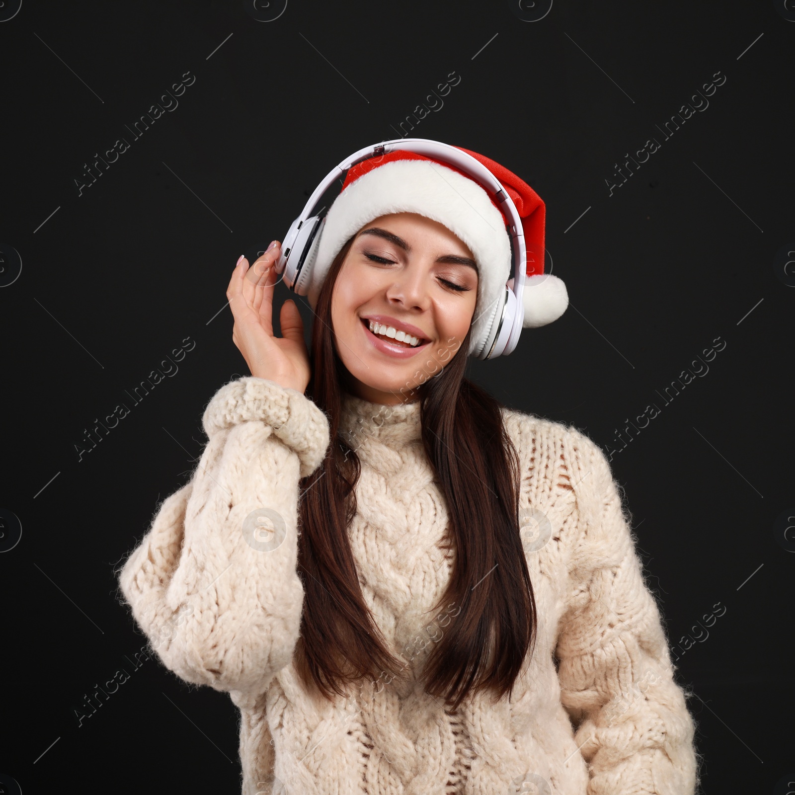 Photo of Young woman in Santa hat listening to Christmas music on black background