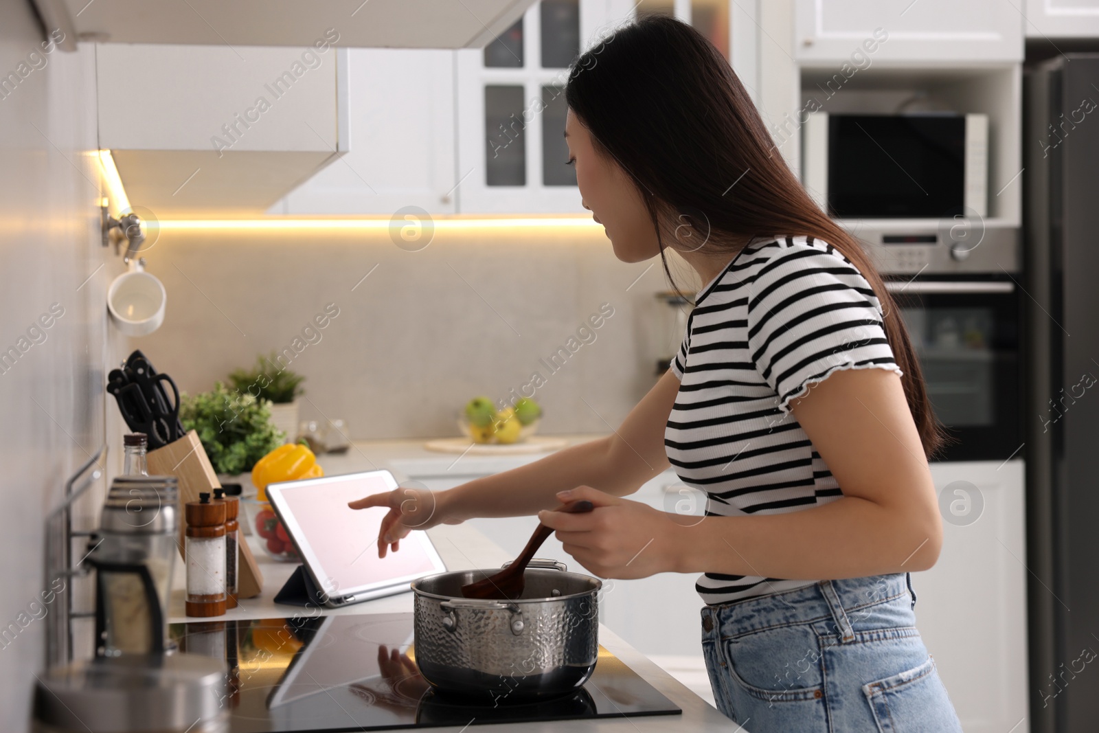 Photo of Woman looking at recipe on tablet while cooking in kitchen