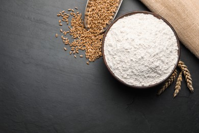 Wheat flour in bowl, spikes and grains on black table, flat lay. Space for text