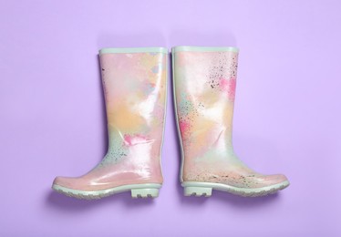 Photo of Pair of colorful rubber boots on violet background, top view