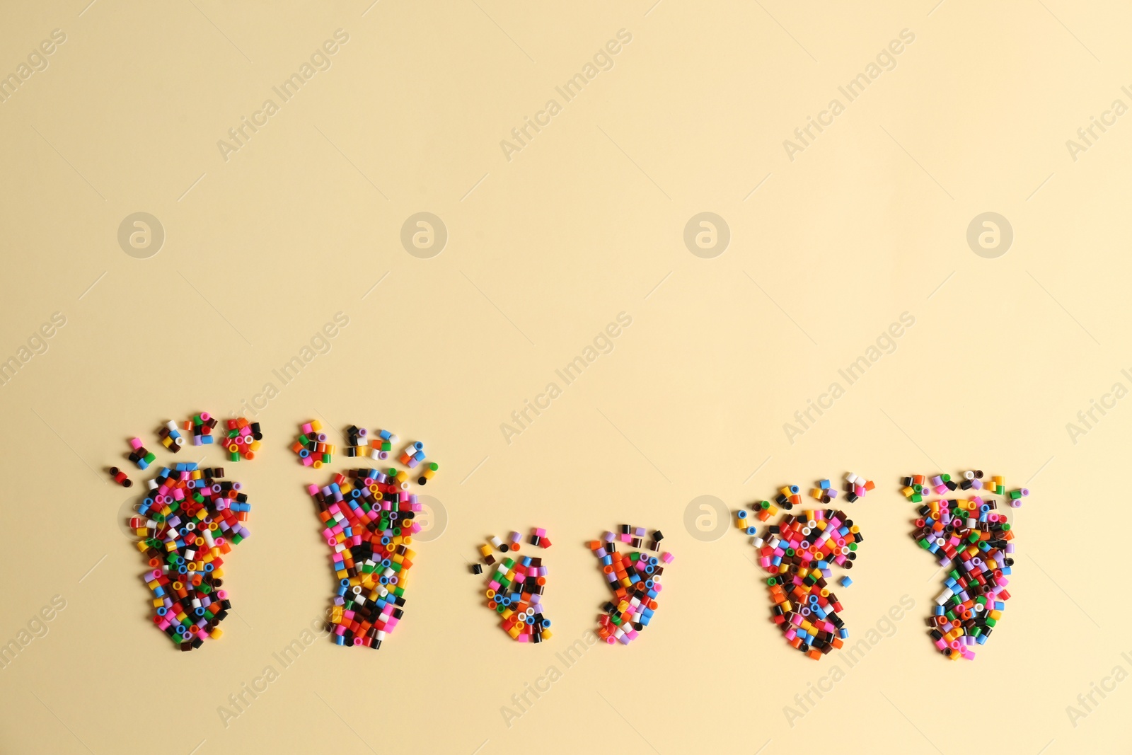 Photo of Family footprints made of melty beads on beige background, flat lay. Space for text