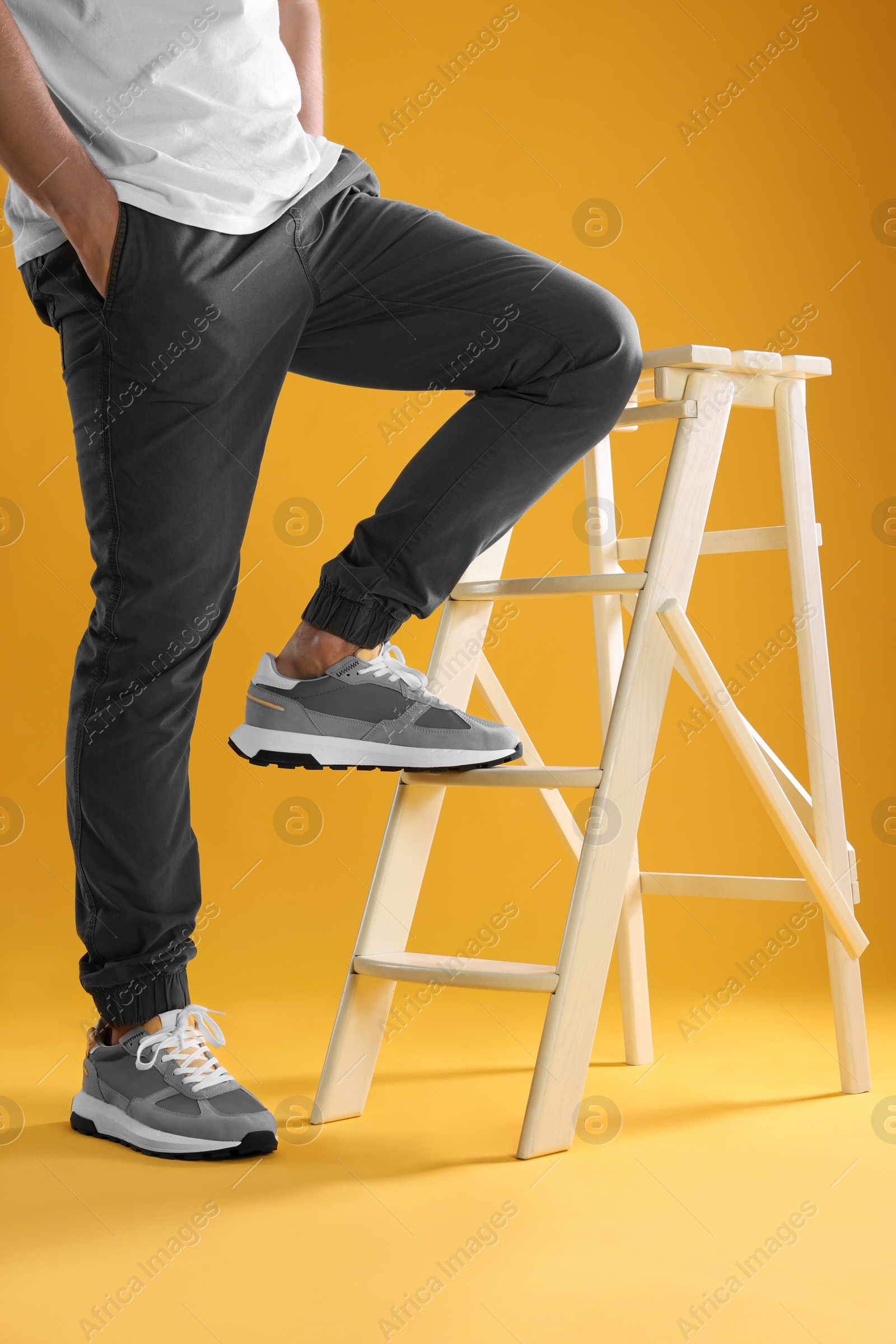 Photo of Man in stylish sneakers standing on white ladder against yellow background, closeup