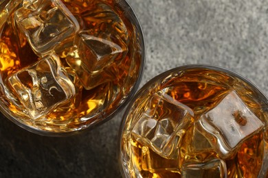 Whiskey and ice cubes in glasses on grey textured table, top view