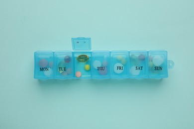 Photo of Plastic box with different pills on light blue background, top view