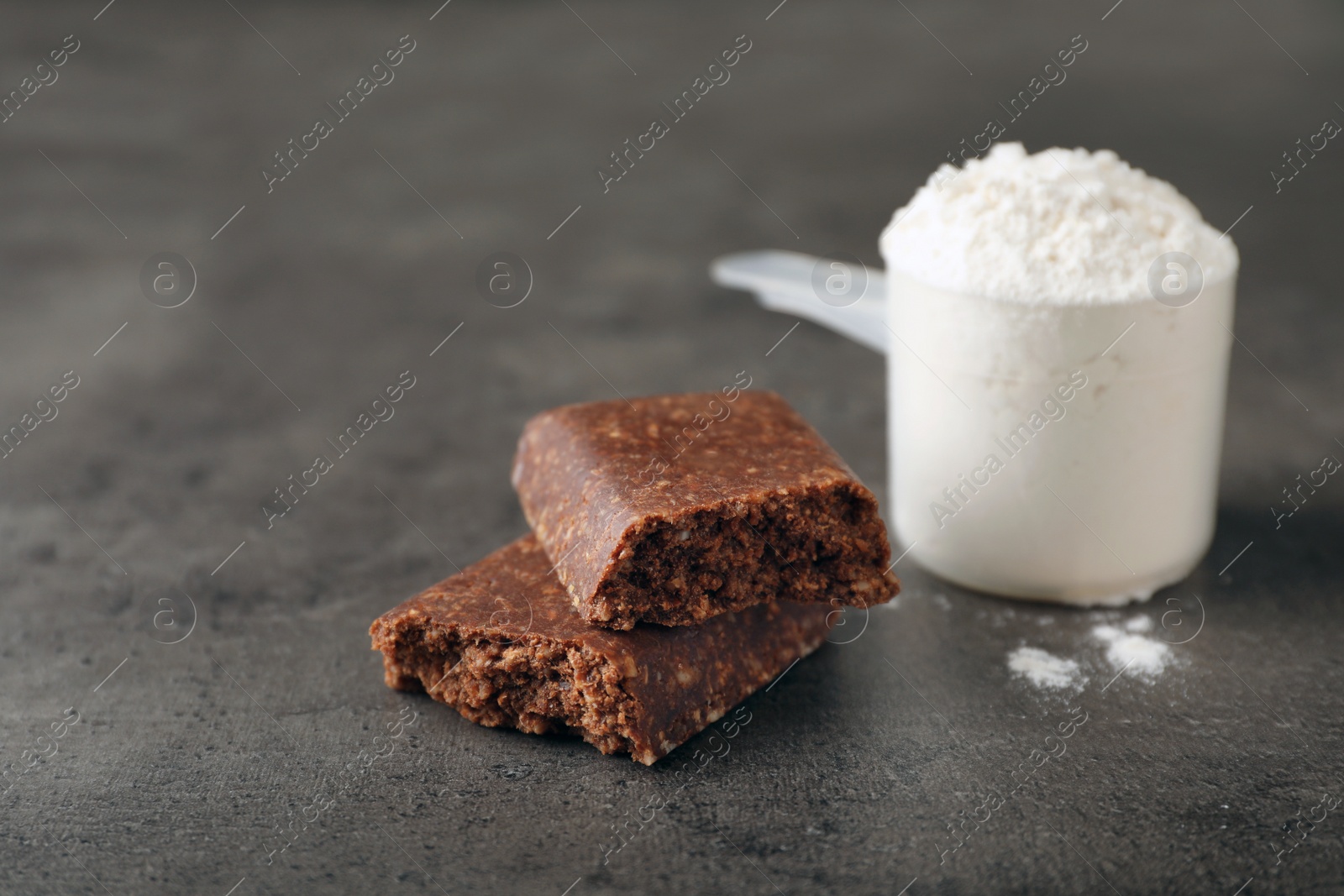 Photo of Tasty protein bar and scoop of powder on grey table. Space for text