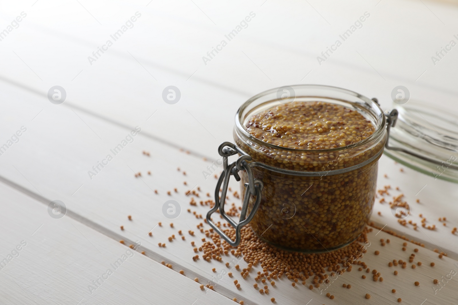 Photo of Jar of whole grain mustard on white wooden table. Space for text