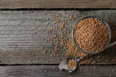 Bowl and spoon of mustard seeds on wooden table, flat lay. Space for text