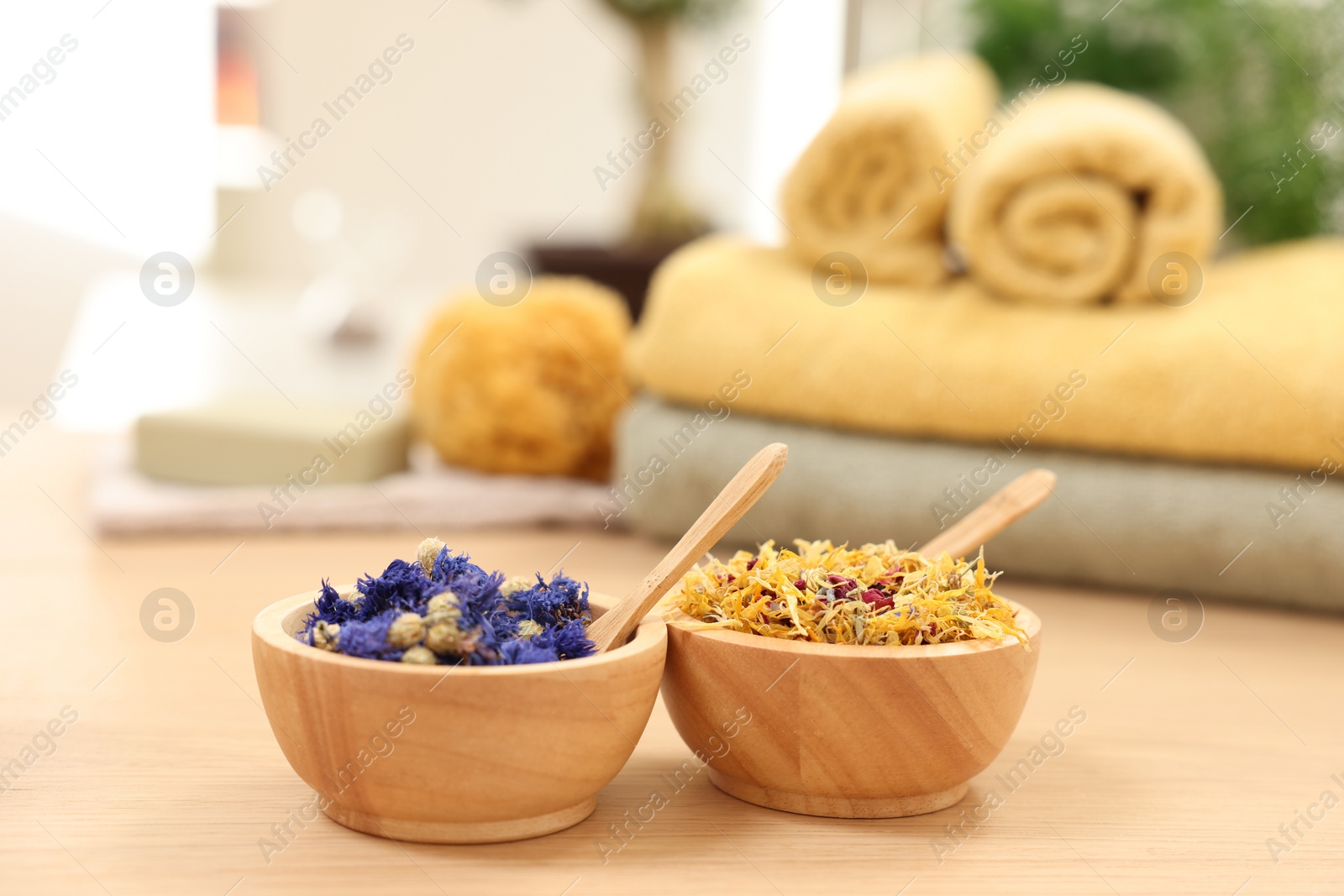 Photo of Bowls with dry flowers and spoons on light wooden table. Spa therapy