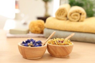 Photo of Bowls with dry flowers and spoons on light wooden table. Spa therapy