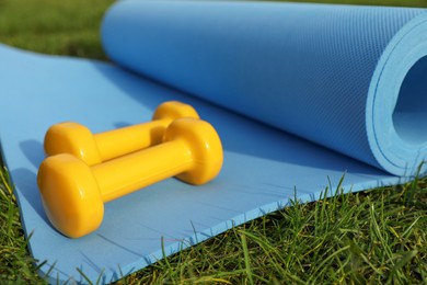 Photo of Dumbbells and fitness mat on green grass outdoors, closeup. Morning exercise
